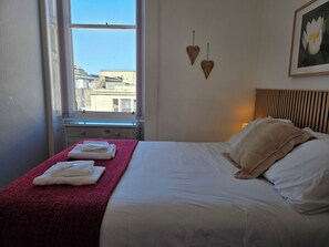 A hotel room with a bed, a window, a red towel, and a wall-mounted picture.