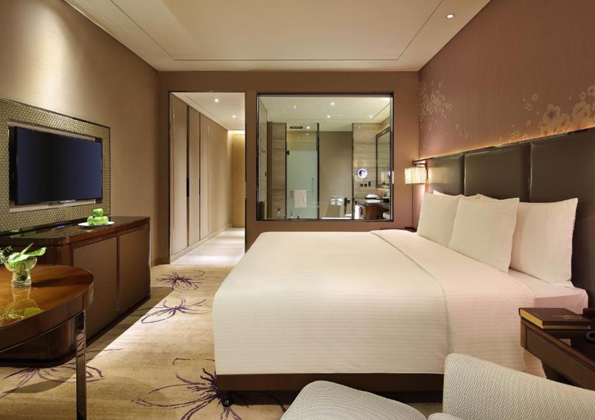 A hotel room with a large bed, a desk with a flat-screen TV, a mirror, and a nightstand.