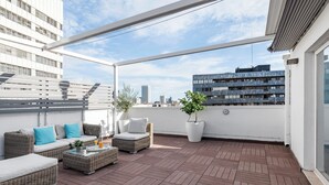 A rooftop terrace with wicker furniture, potted plants, and a view of city buildings. - Smart Cuzco Castellana Penthouse (Madrid)