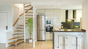 A modern kitchen with a stainless steel refrigerator, oven, and microwave. There is a wooden staircase with a potted plant. - Smart Cuzco Castellana Penthouse (Madrid)