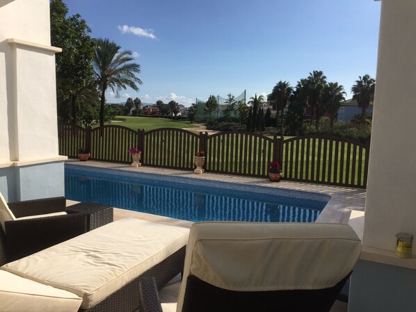 A pool area with lounge chairs and a view of a golf course.