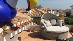 En tagterrasse med en stor, oppustelig flamingo, en fletsofa og terracotta tagsten.