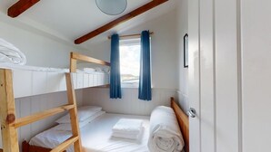 A bunk bed room with white bedding, a wooden ladder, and a window with blue curtains.