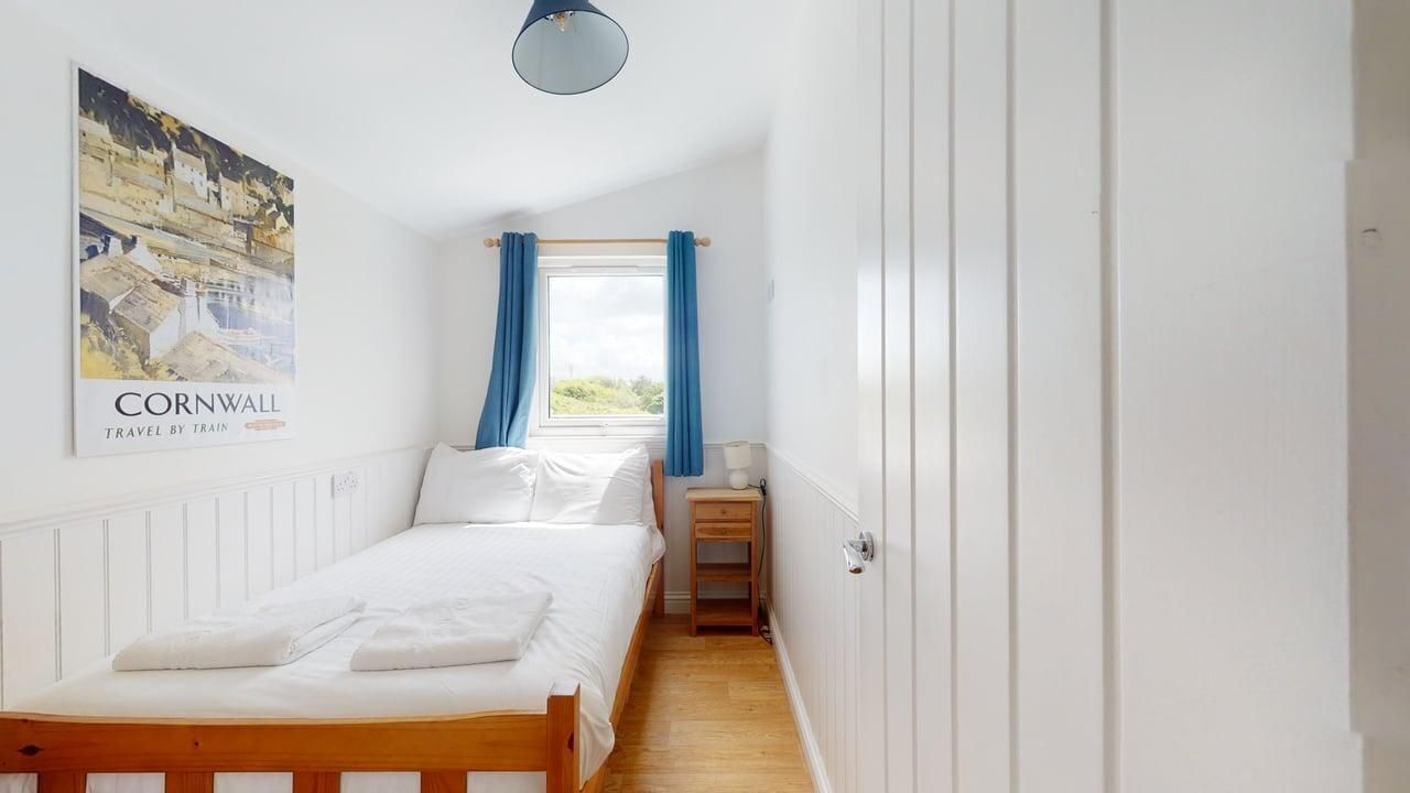 Ein Schlafzimmer mit einem hölzernen Bett, weißer Bettwäsche, einem Nachttisch, einer Lampe, einem Fenster mit blauen Vorhängen und einem Poster an der Wand.