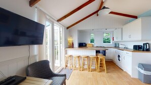 A modern kitchen with white cabinets, a large TV, wooden stools, and a bar area.