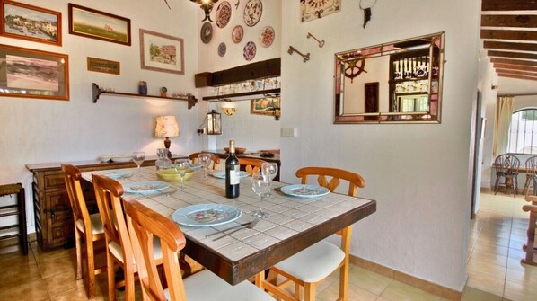 A dining area with a large wooden table set for four, surrounded by wooden chairs. There are framed pictures and decorative plates on the walls. - Rustic Villa with pool Marquesa WS (Denia)