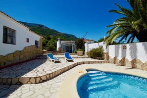 Un espace piscine comprenant deux chaises longues, une terrasse dallée de pierres et une piscine à l’eau d’un bleu cristallin.