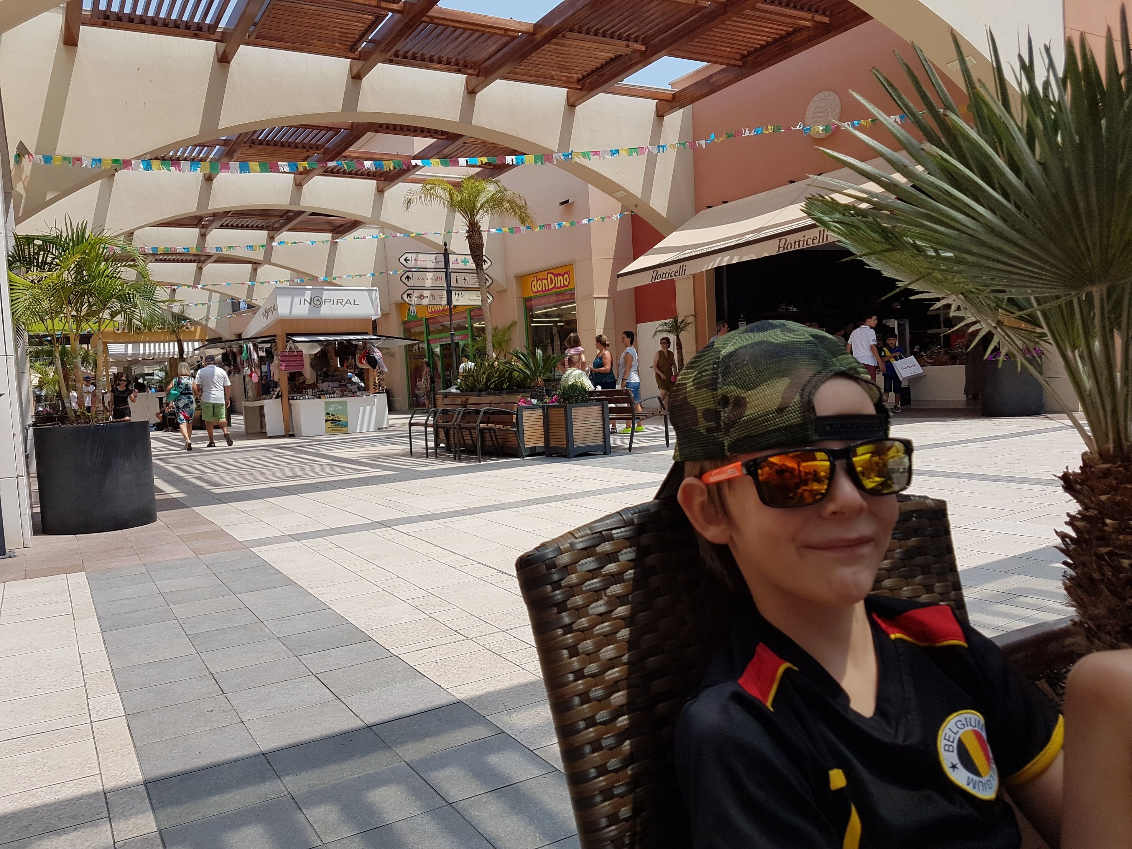 A covered outdoor area with tiled flooring, benches, and potted plants.