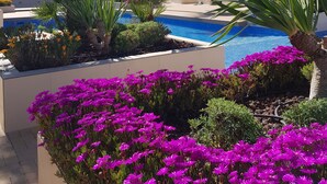 Ett hotell med en swimmingpool omgiven av palmer och färgstarka blommor.