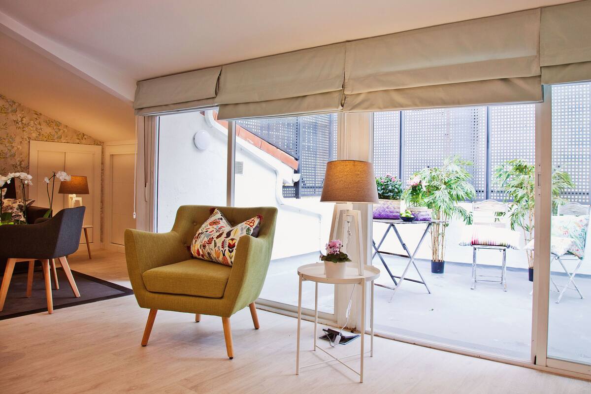 A modern living room with a green armchair, a side table with a lamp, and a view of the outside balcony area.