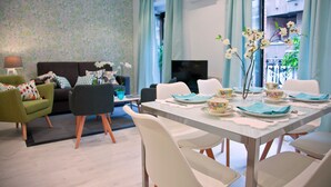 Uma sala de estar moderna com área de jantar, apresentando um sofá, cadeiras, uma TV e uma mesa posta para refeições.