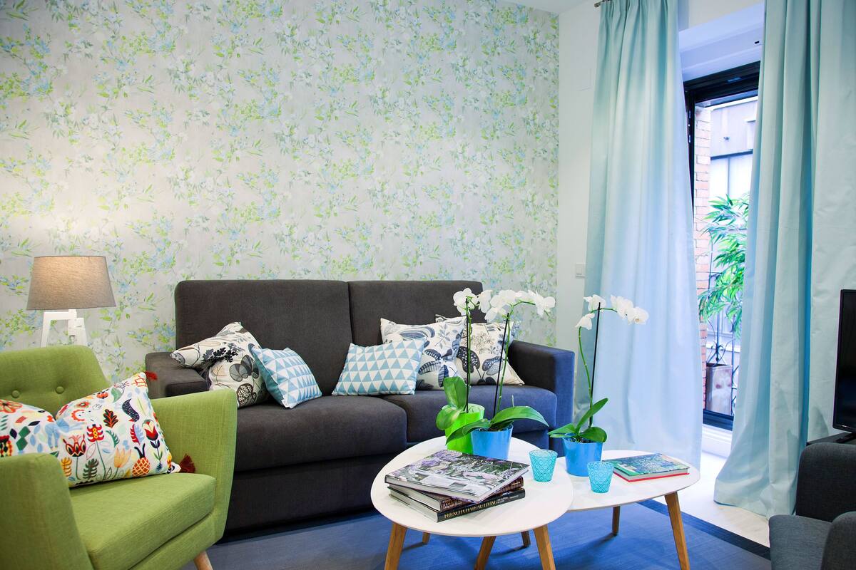 A living room with a sofa, green armchair, and a coffee table with books and a lamp.
