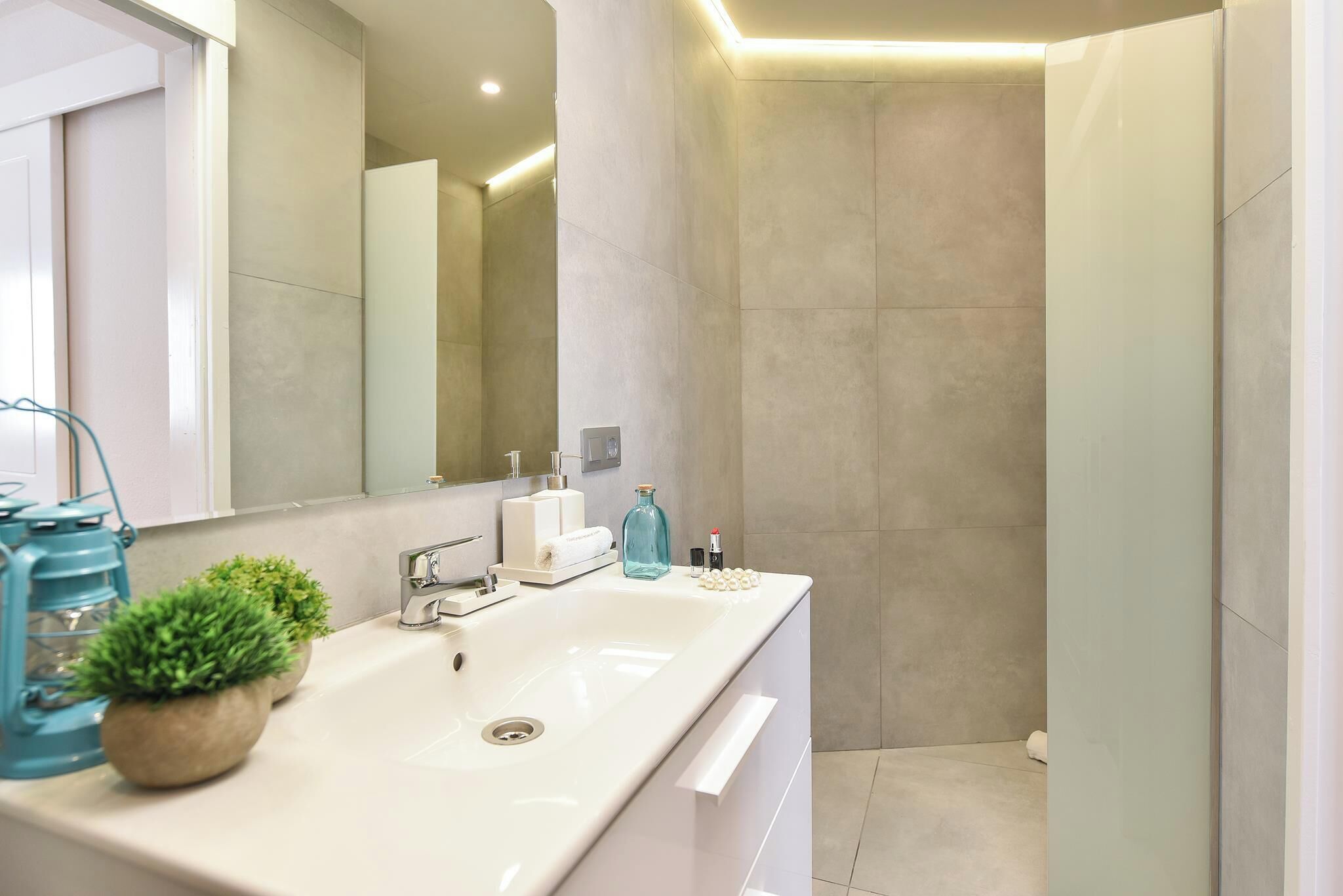 A modern bathroom with a white sink, mirror, and shower area.
