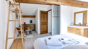 Camera da letto con un letto, una scala in legno, una scrivania con una sedia, un armadio in legno e un bagno con doccia.