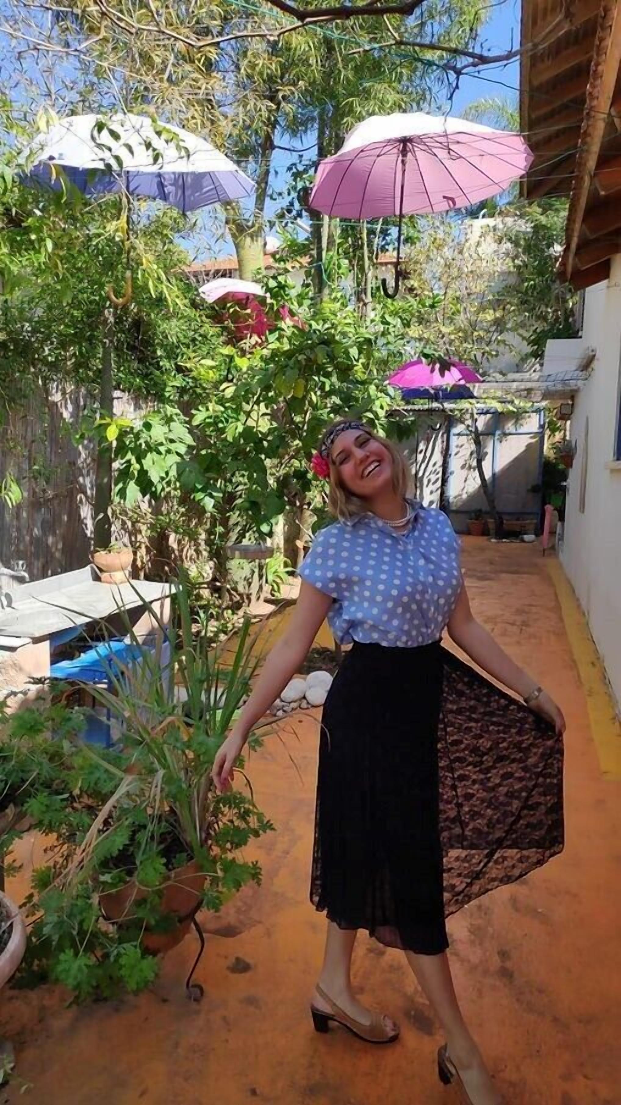 A person standing in a courtyard with potted plants and umbrellas.