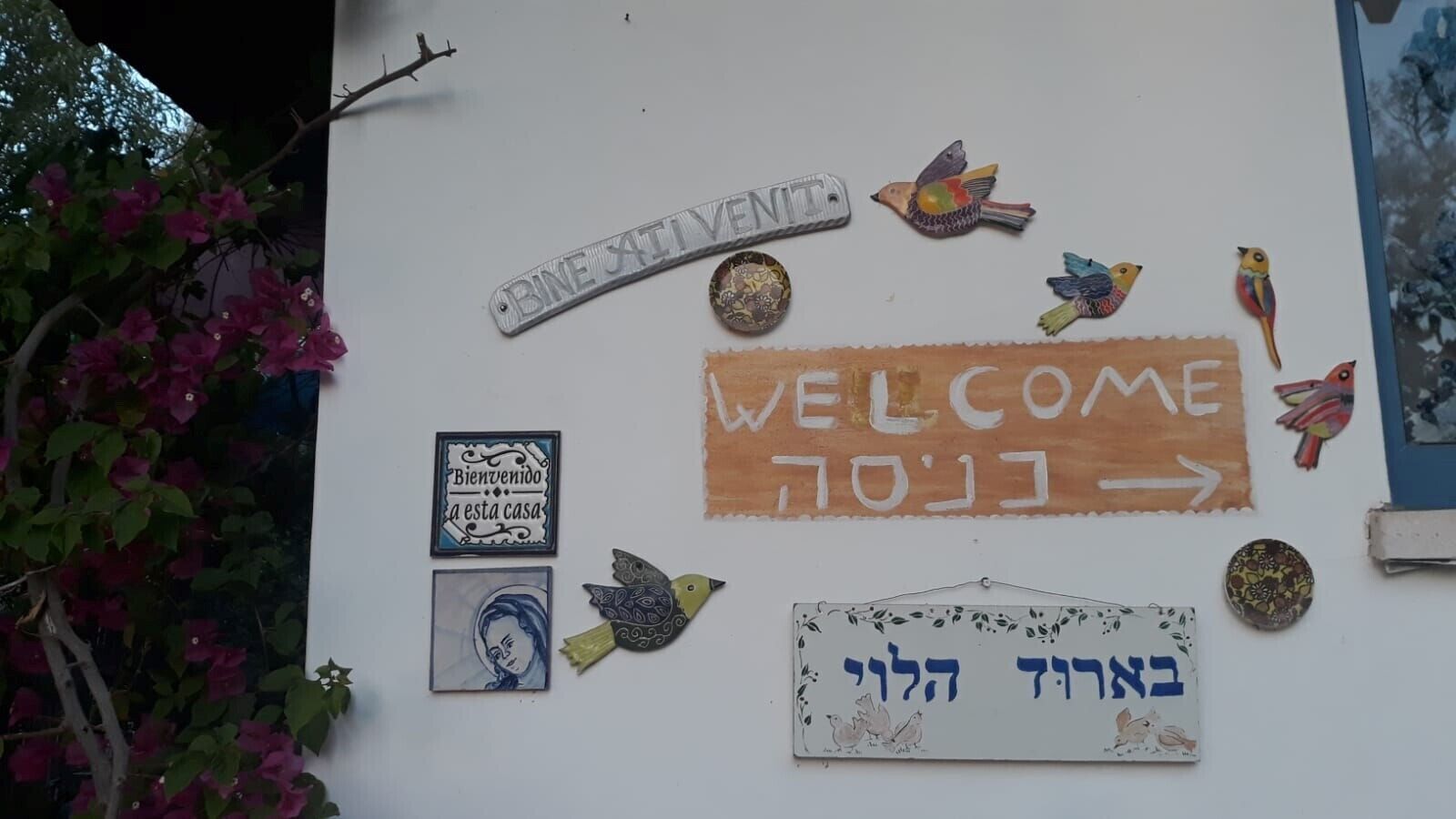 A wall with various welcome signs, including a 'Welcome' sign in English and Hebrew, and a 'Bienvenidos' sign in Spanish.