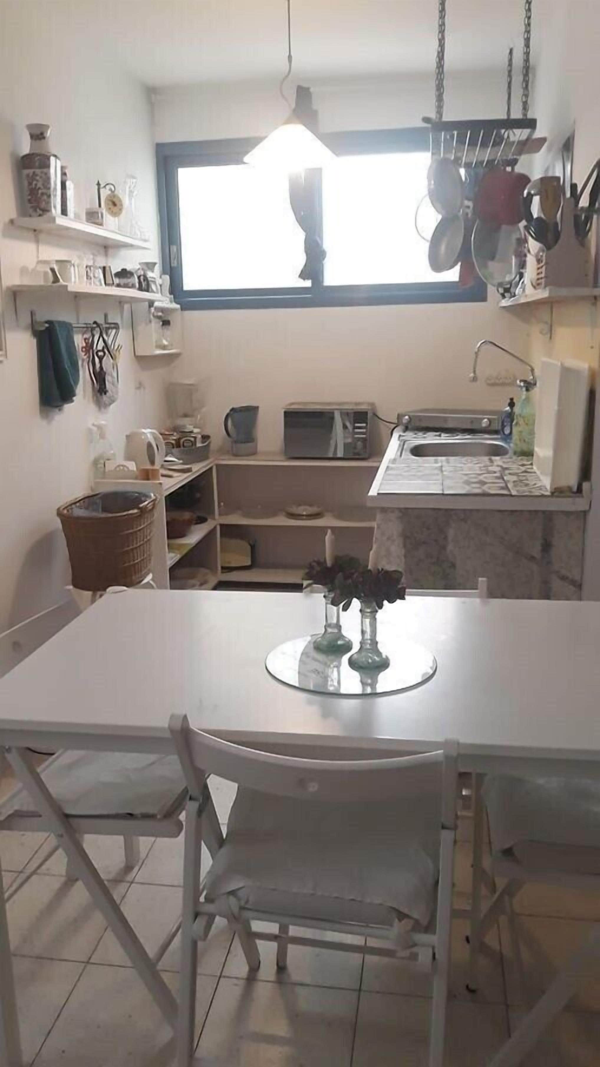 A compact kitchen with a dining table, chairs, a hanging pot rack, and a window providing natural light.