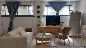 Una sala de estar acogedora con un sofá, una mesita redonda, un televisor y un refrigerador.
