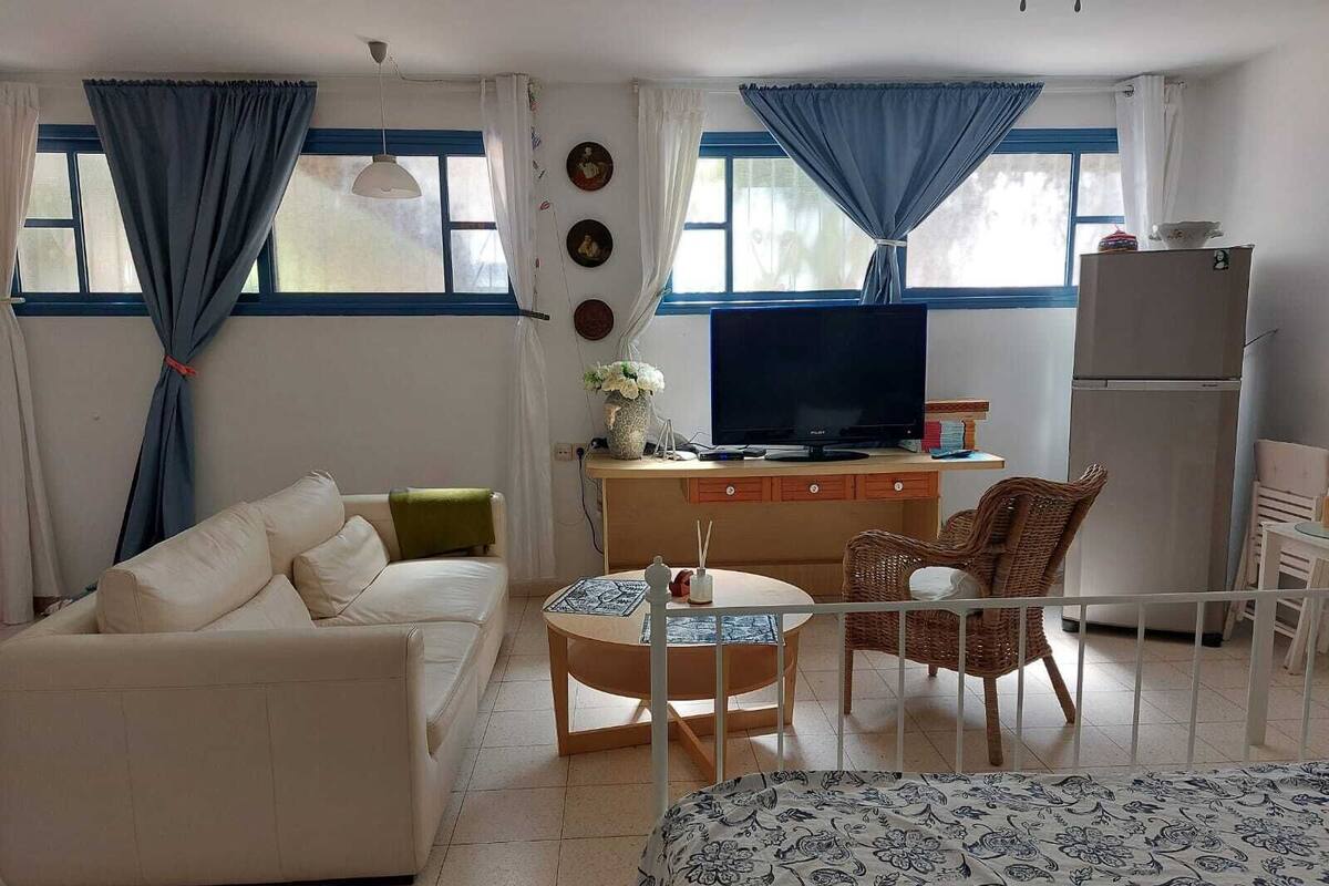 A cozy living room with a sofa, a small round table, a television, and a refrigerator.