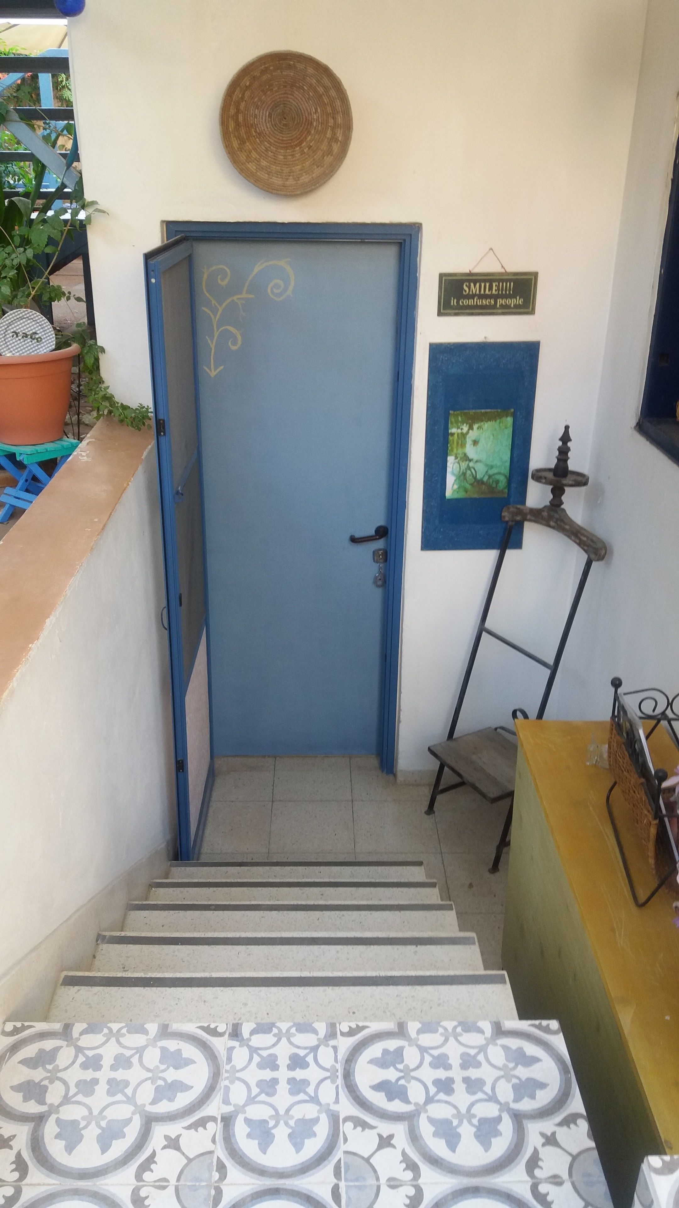 A blue door with a sign above it, a staircase leading to a room, and a wall-mounted picture.