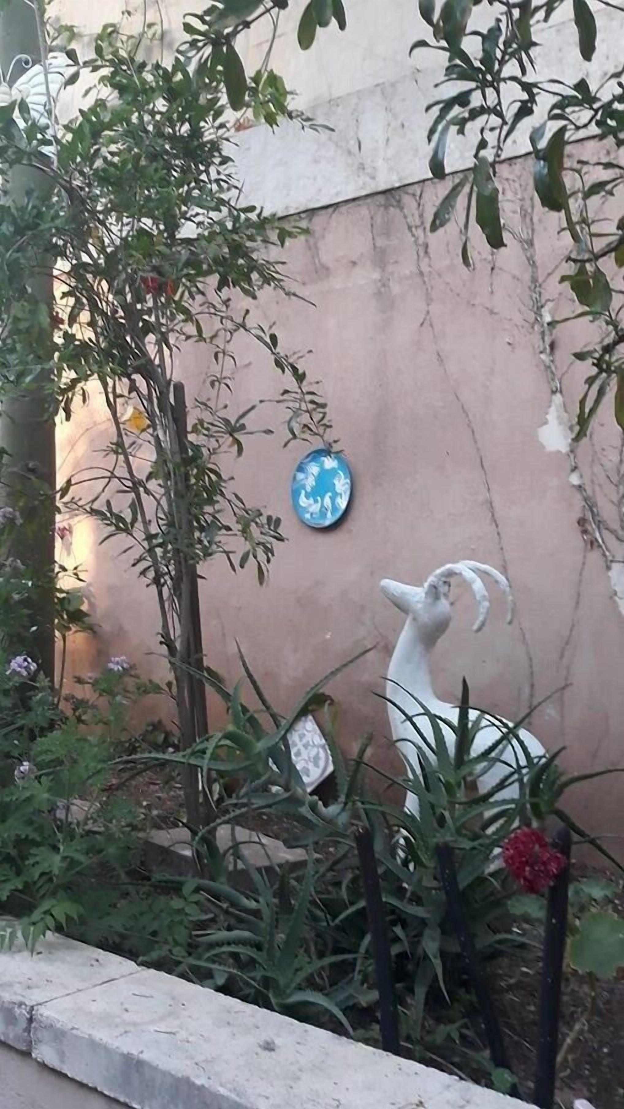 A garden with a white bird sculpture, a blue decorative plate, and various plants.