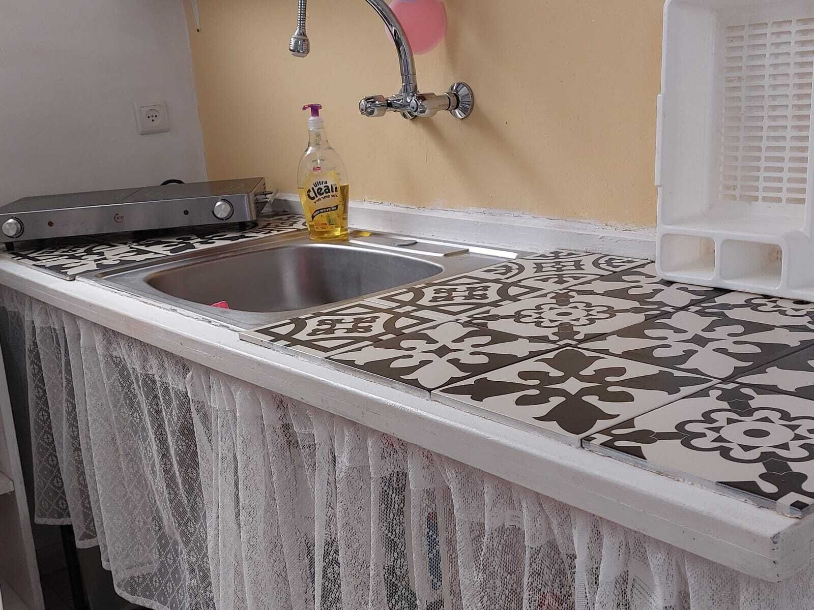 A kitchen with a sink, a bottle of hand soap, and a patterned backsplash.