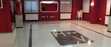 A spacious lobby with a polished floor, a large H+V logo, and a red wall with a window and radiator.