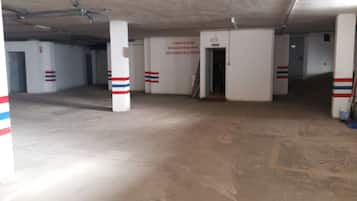 Eine leere Tiefgarage mit weißen Säulen, die mit roten und blauen Streifen gekennzeichnet sind, einem Betonboden und einer Tür zu einem weiteren Bereich.