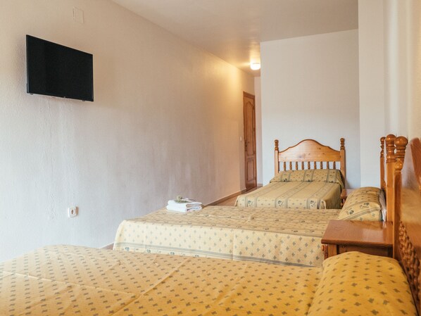 A bedroom with two beds, a wooden headboard, and a flat-screen TV mounted on the wall. - Hotel Valmar (Villar de Olalla)