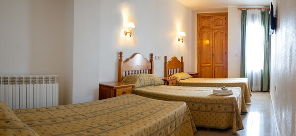 Habitación de hotel con dos camas individuales, un armario de madera, un radiador y dos lámparas de pared.