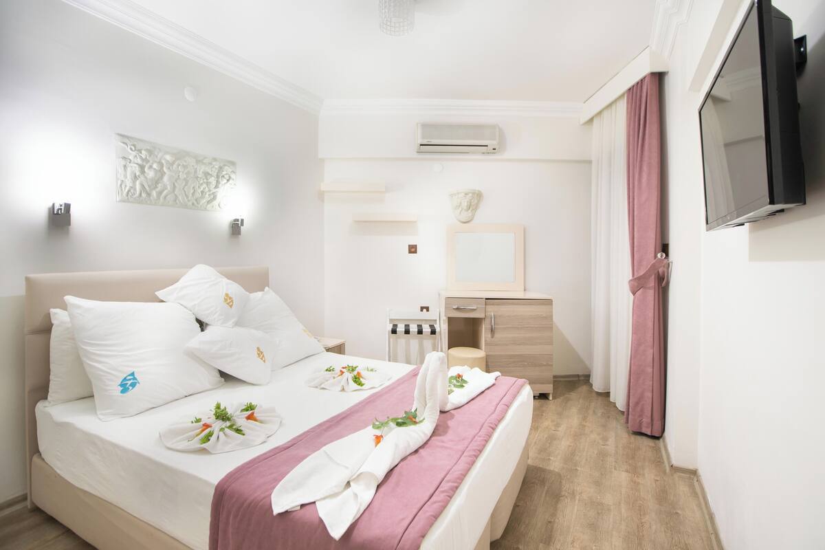 A hotel room with a bed, bedside table, mirror, and a TV mounted on the wall.