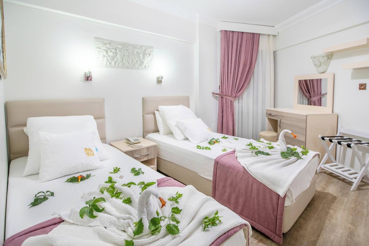 A hotel room with two beds, a desk, a vanity, and a shower area.