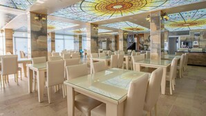 A spacious dining area with glass tables and chairs, a high ceiling with a stained glass design, and a modern interior. - Sea Bird Hotel (Didim)