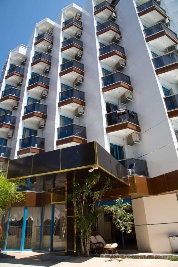 A multi-story residential building with balconies, a glass entrance, and outdoor seating.