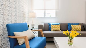 A living room with a blue armchair, a grey sofa with patterned cushions, a white coffee table, and a vase with yellow flowers. - The Viso Smart III (NEW) (Madrid)