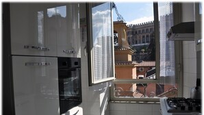 Eine Küche mit weißen Schränken, einem schwarzen Backofen und einem Fenster mit Blick auf ein Gebäude mit einem Balkon.