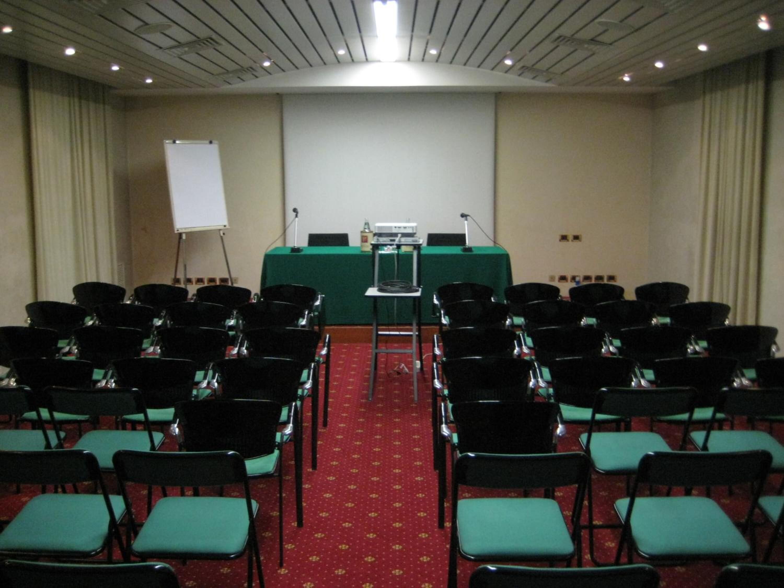 A conference room with rows of chairs, a podium, and a whiteboard.