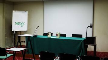 Une salle de conférence équipée d’un tableau blanc, d’un écran de projection et d’une table avec des chaises.