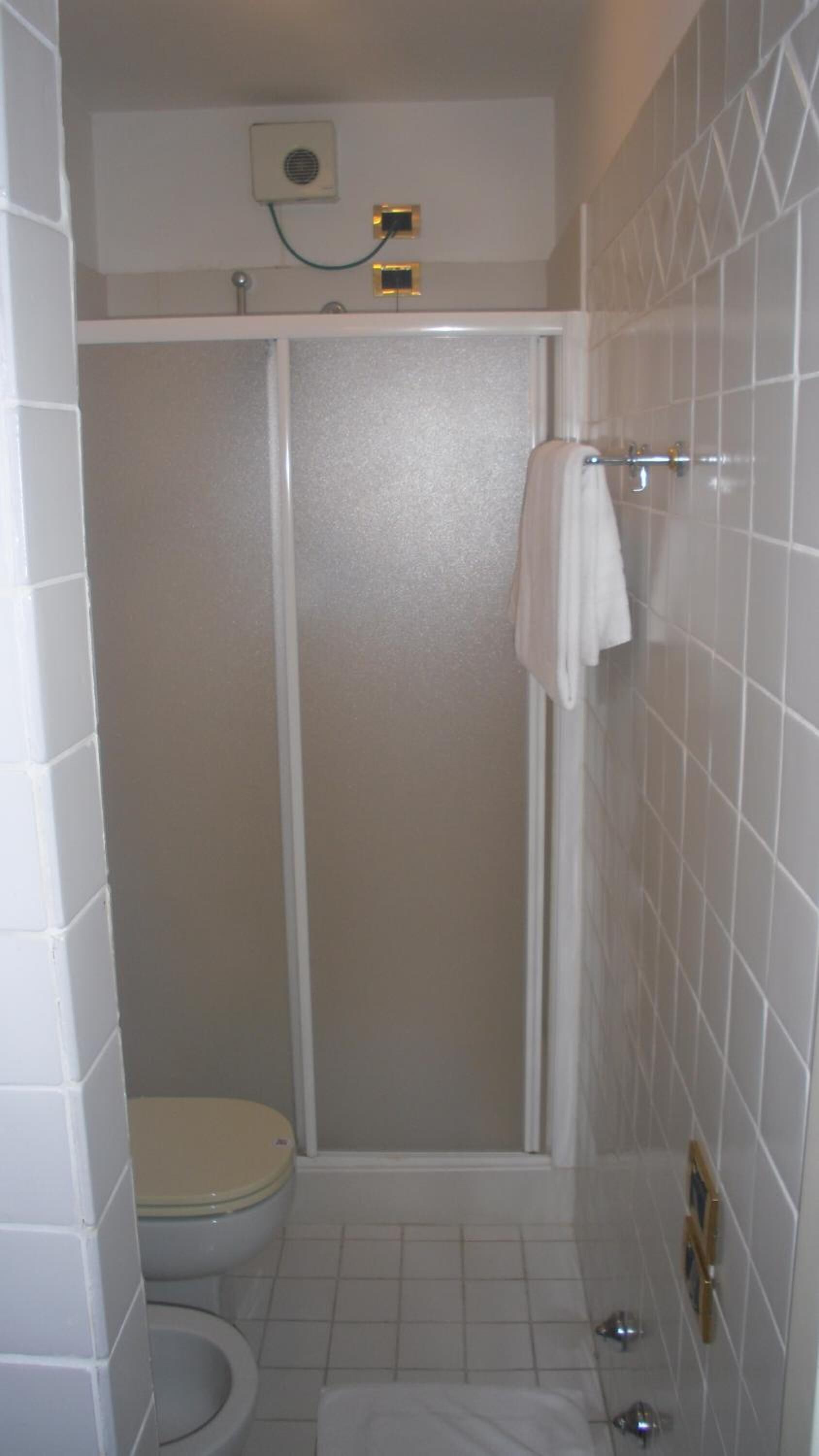 Une petite salle de bain fermée, comprenant des toilettes, un espace douche et une serviette suspendue à un porte-serviettes.