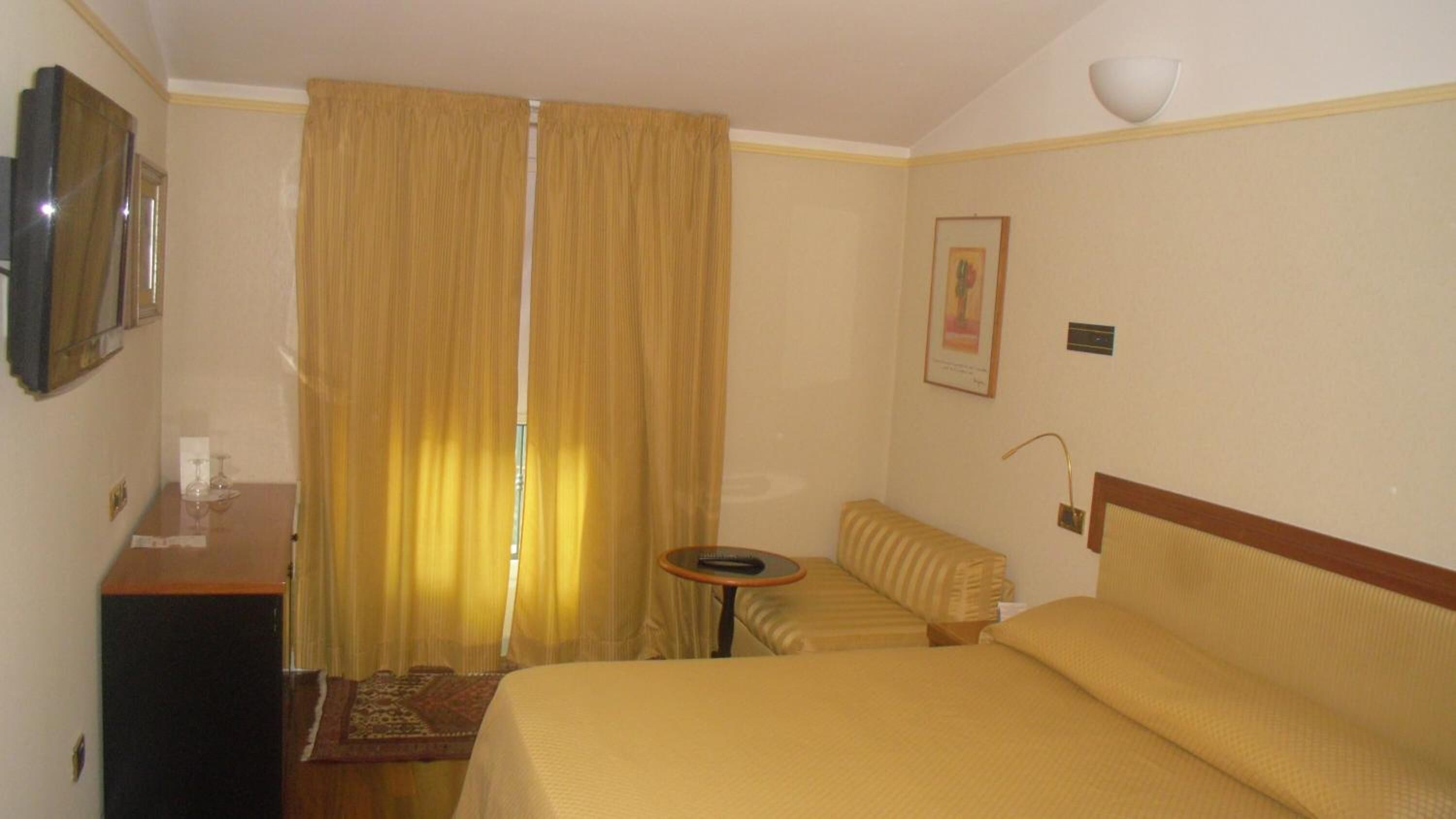 A hotel room with a bed, a small table, a sofa, a desk, and a television.