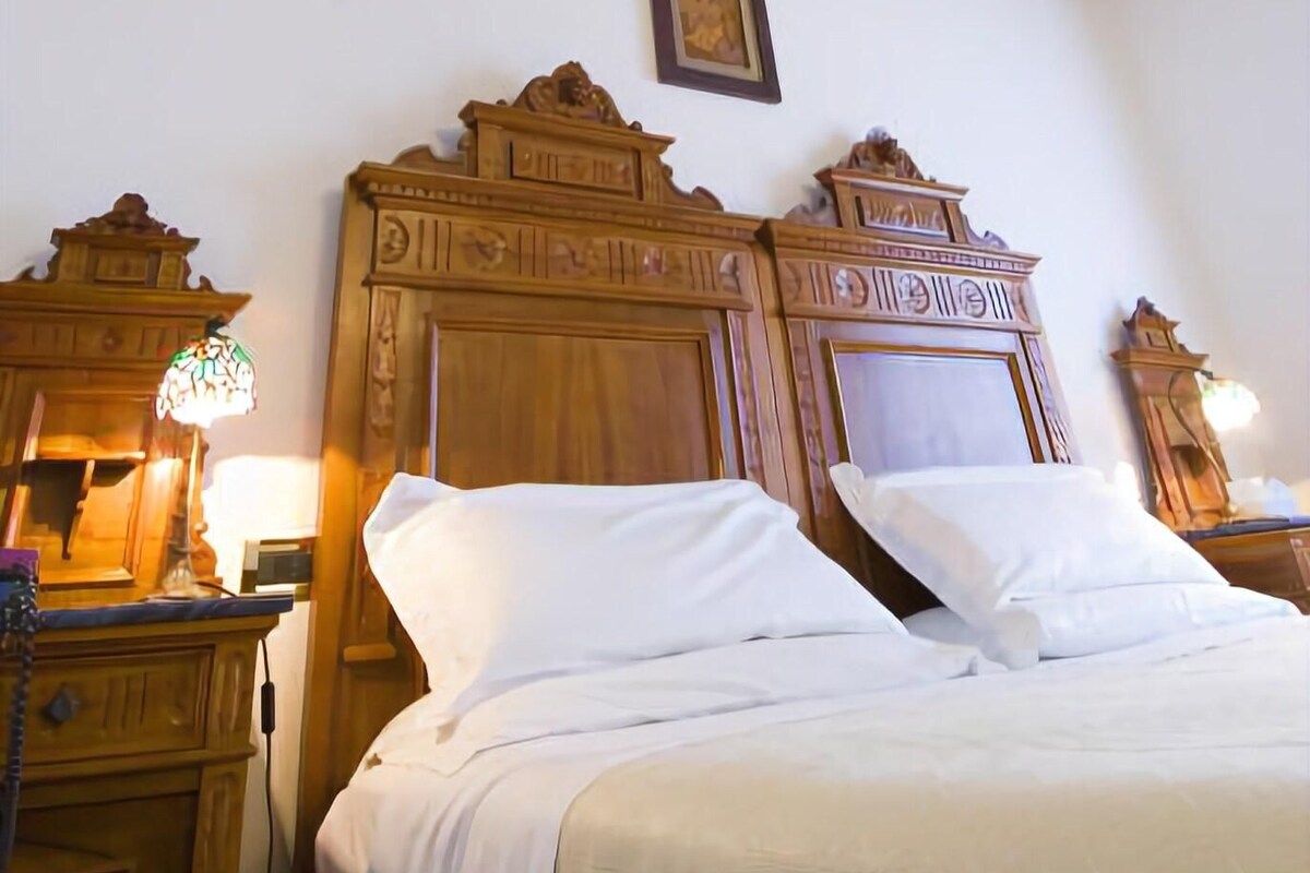 A bedroom with a large bed, wooden headboard, and a ceiling mural.