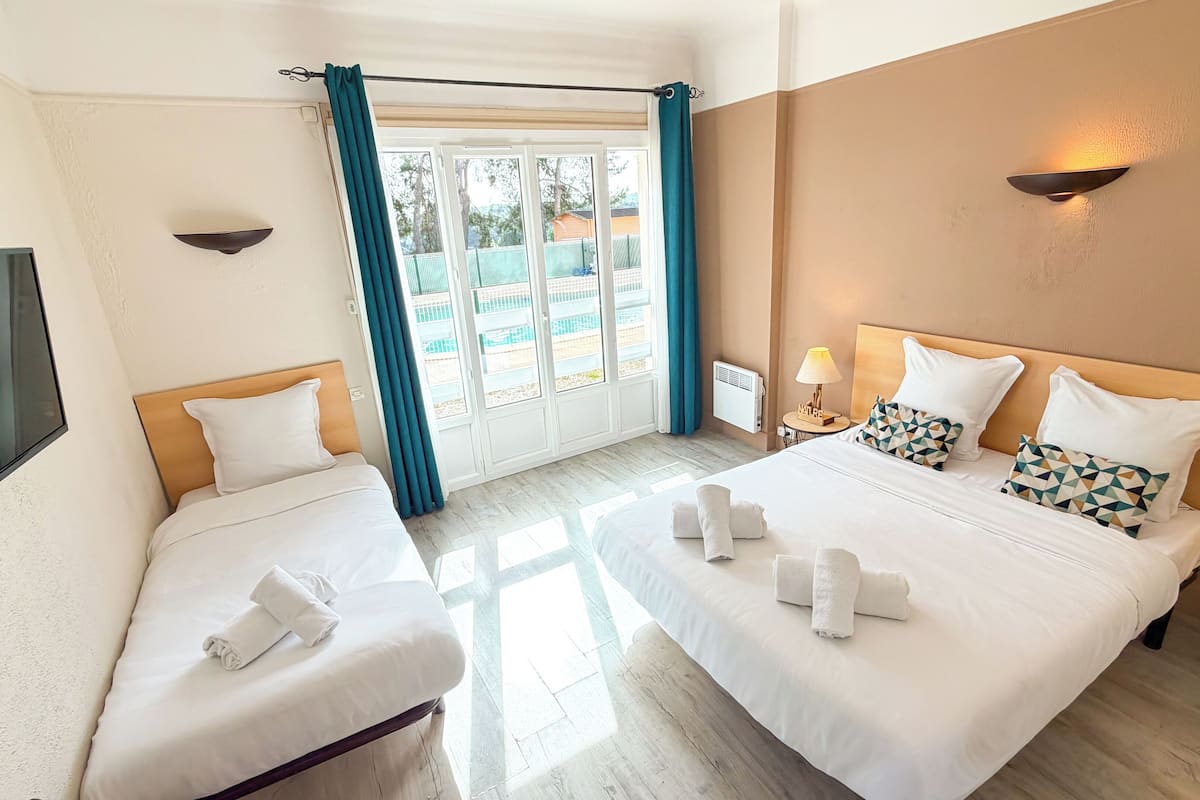 A hotel room with two beds, a TV, a window with curtains, and a view of the outside.