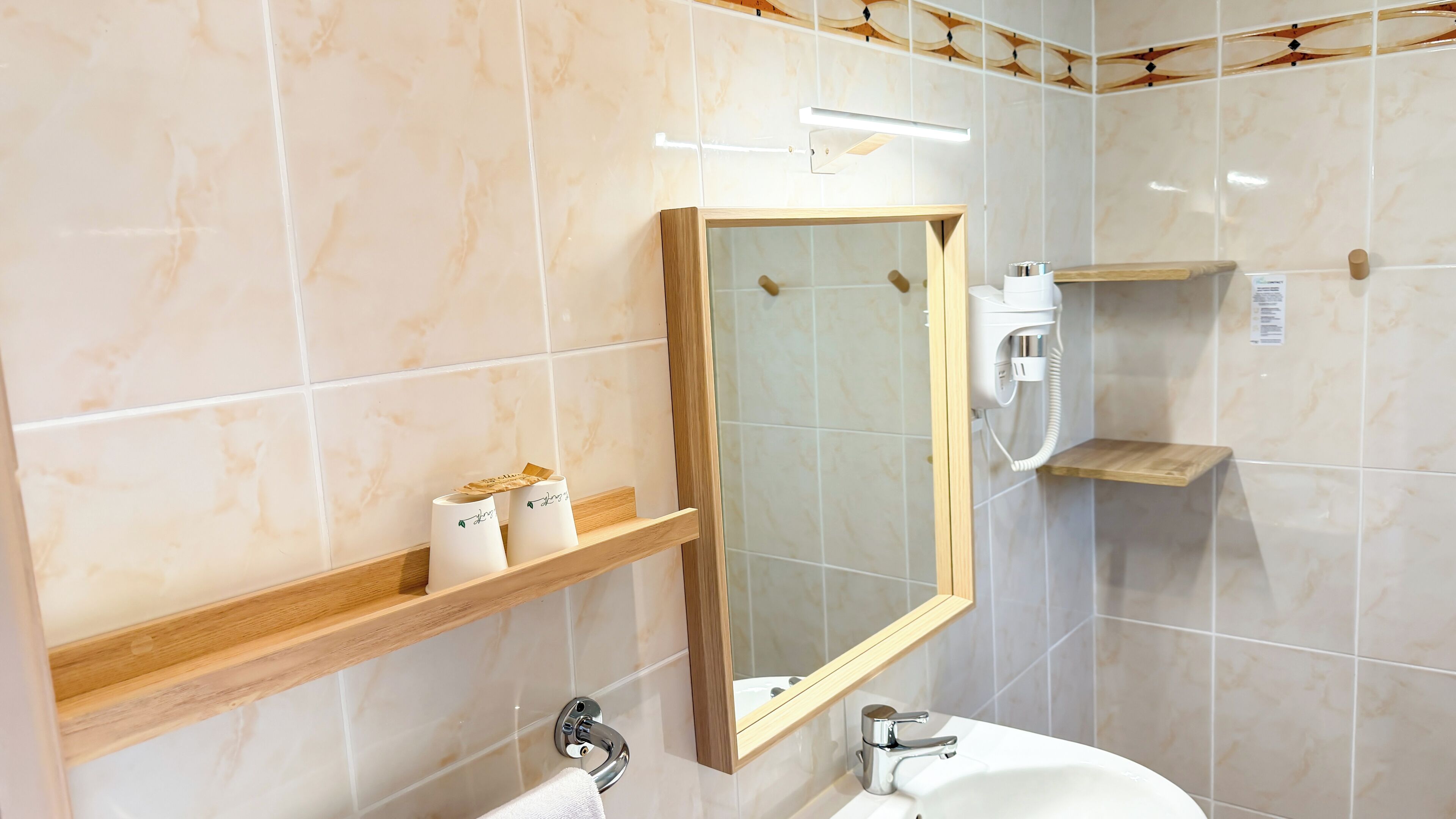 A bathroom with a marble-tiled wall, a wooden shelf with toiletries, a mirror, a sink, and a handheld showerhead.