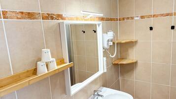 A bathroom with a mirror, a sink, and a shower. There are wooden shelves with toiletries.