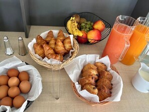 A breakfast table with croissants, eggs, a fruit basket, and a glass of orange juice.