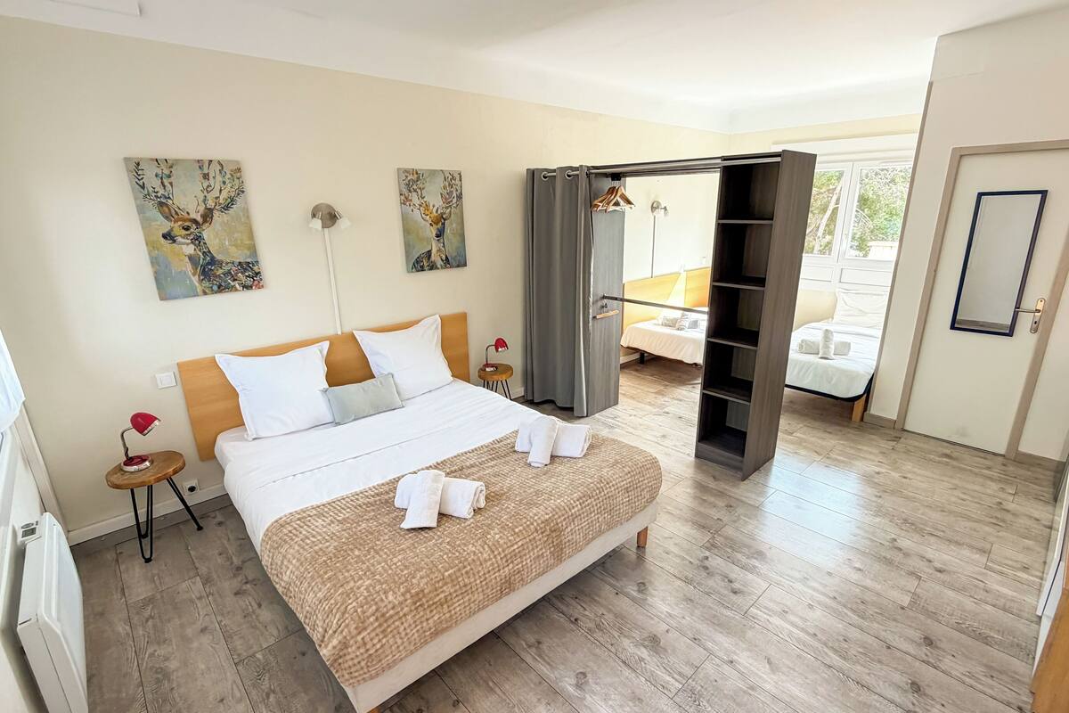 A hotel room with a large bed, a wardrobe, a bedside table with a lamp, and artwork on the walls.