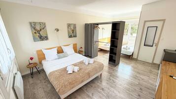 A hotel room with a large bed, a wardrobe, a bedside table with a lamp, and artwork on the walls.