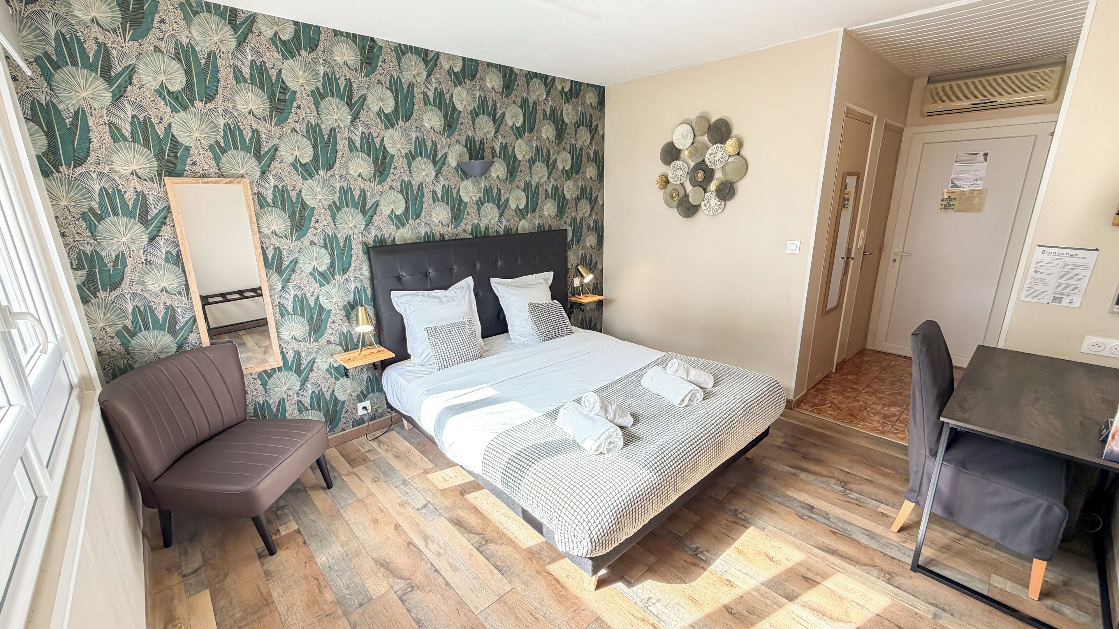 A hotel room with a large bed, a chair, a desk, and a mirror.