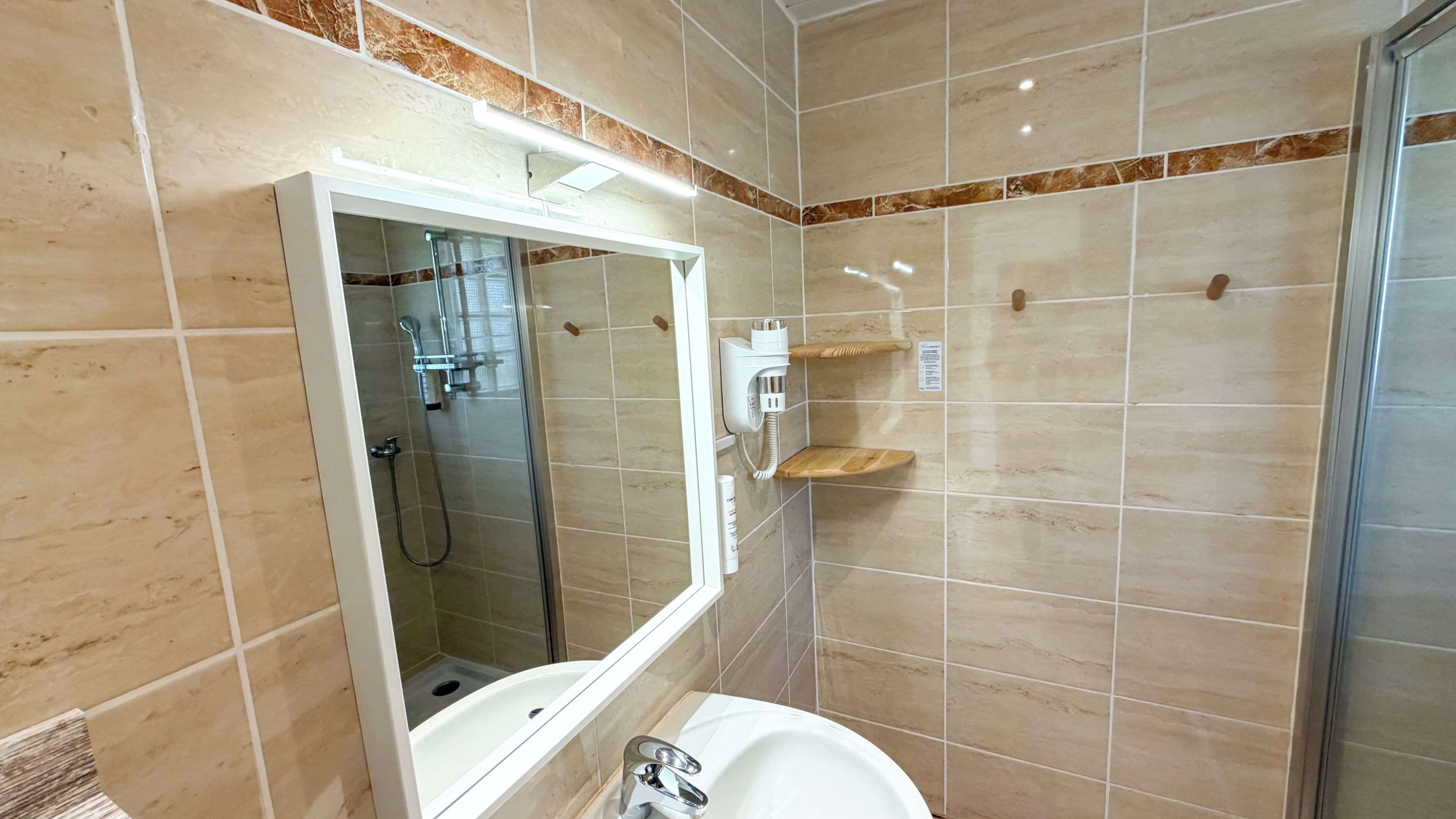 Een moderne badkamer met een douche met glazen wanden, een witte wastafel en een spiegel.