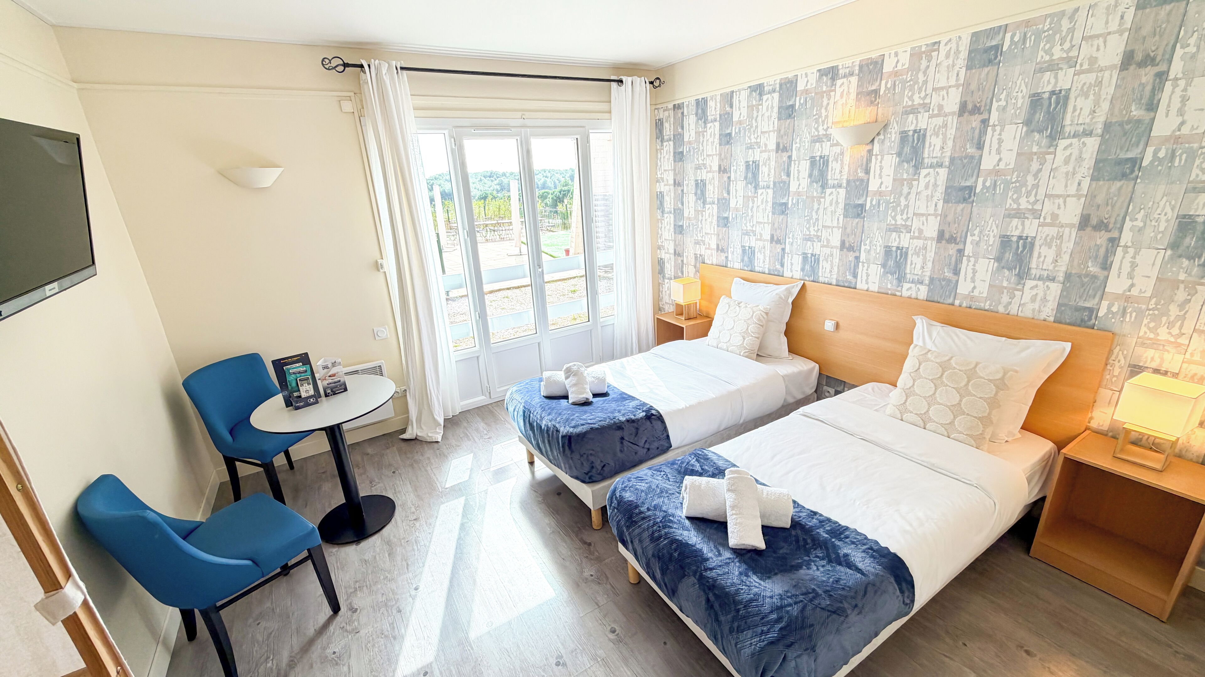 A hotel room with two beds, a desk, a chair, and a view of the outdoors.